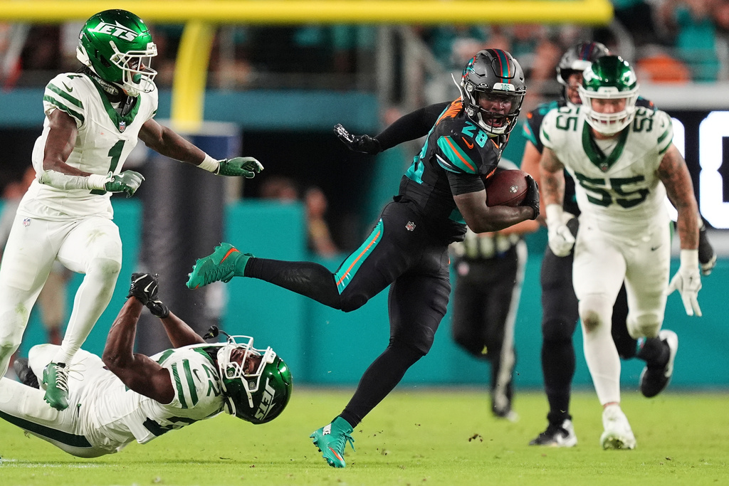 Miami Dolphins running back De'Von Achane (28) breaks tackle attempts by New York Jets' Sauce Gardner (1) and Tony Adams (22) as Braiden McGregor (55) gives chase in the second half of an NFL football game, Monday, Sept. 29, 2025, in Miami Gardens, Fla. (AP Photo/Rebecca Blackwell)