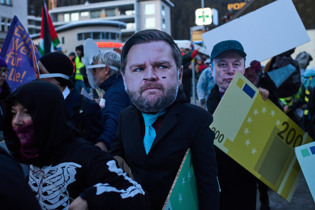 People with masks on Elon Musk, center, and United States Vice President JD Vance, right, attend a demonstration against the United President Donald Trump and the Annual Meeting of the World Economy Forum in Davos, Switzerland, Sunday, Jan. 18, 2026. (AP Photo/Markus Schreiber)