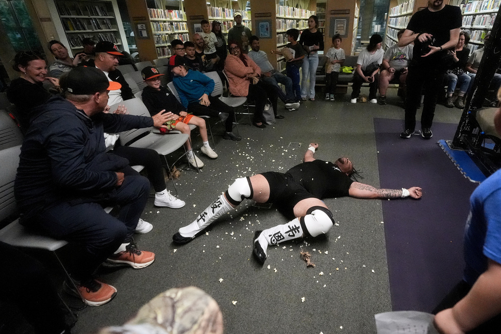 Fans watch as wrestler Hitman Wayne lies on the ground after losing a match against Rufio Banderas during a Lucha Libro pro wrestling event at Benicia Public Library Saturday, May 2, 2026, in Benicia, Calif. (AP Photo/Jeff Chiu)