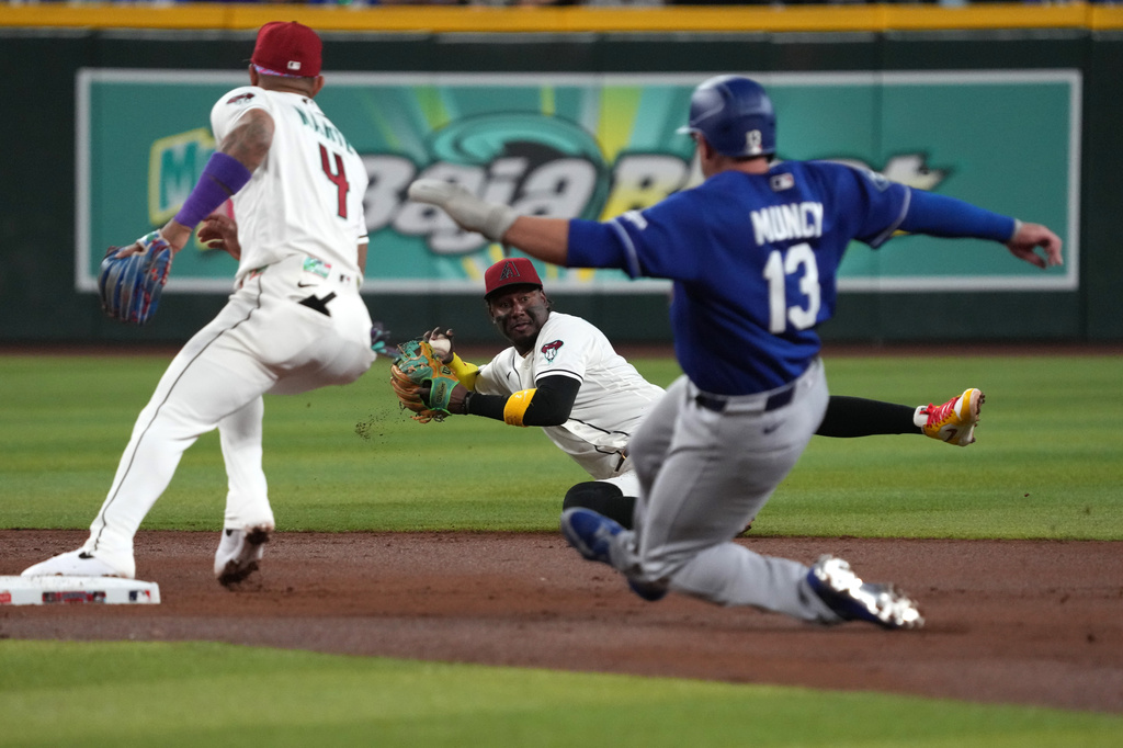Arizona Diamondbacks shortstop Geraldo Perdomo, center, tries to make a play from the ground against the Los Angeles Dodgers in the second inning of a baseball game, Monday, June 1, 2026, in Phoenix. (AP Photo/Rick Scuteri)
