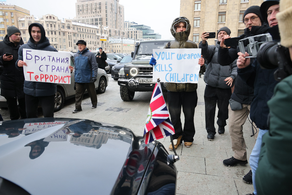 Demonstrators stand with posters, one of them reading "Britain is a terrorist country" next to the U.K. Charge d'Affairs to Russia, Danae Dholakia's limousine as she arrives at the Russia's Foreign Ministry, in Moscow, Russia, Thursday, Jan. 15, 2026. (AP Photo)