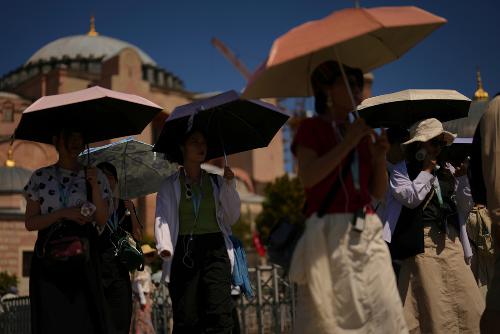 FILE - Tourists use umbrellas to shelter against the sun outside Hagia Sophia mosque during a hot summer day in Istanbul Aug. 12, 2025. (AP Photo/Francisco Seco, File)