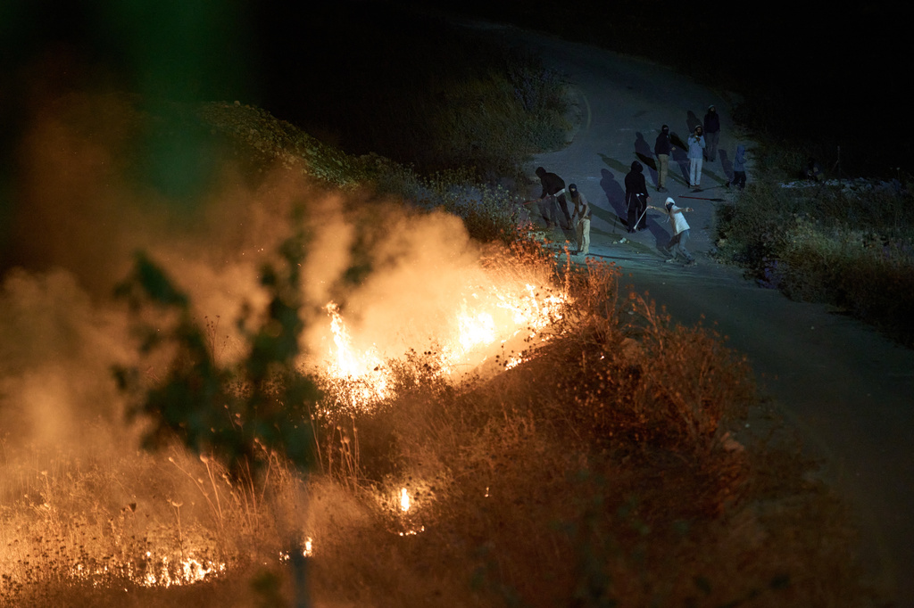 Israeli settlers use slingshots to hurl stones as brush burns along a roadside after Palestinians set it ablaze to prevent the settlers from approaching the West Bank village of Sinjil, Friday, July 17, 2026. (AP Photo/Leo Correa)