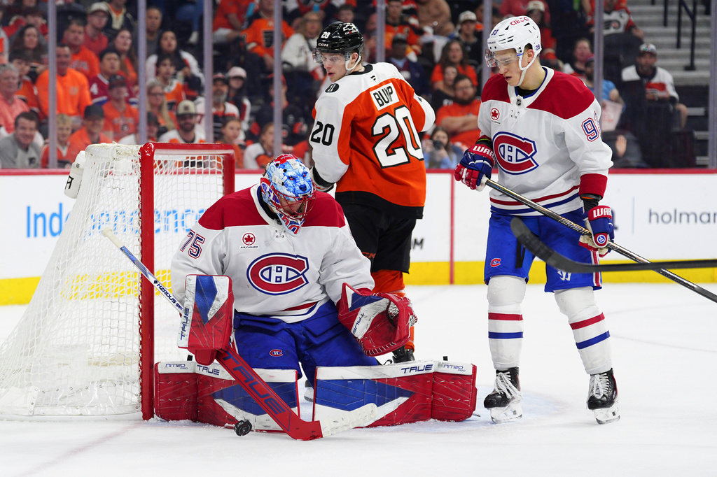 Montréal Canadiens goaltender Jakub Dobes, left, makes a save past Ivan Demidov (93) and Philadelphia Flyers' Alex Bump (20) during the second period of an NHL hockey game, Tuesday, April 14, 2026, in Philadelphia. (AP Photo/Derik Hamilton)
