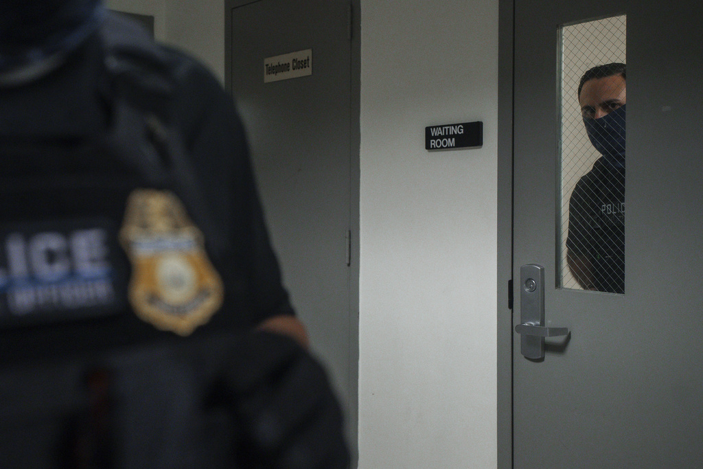 An Immigration and Customs Enforcement agent peers through a door while waiting to detain respondents inside the waiting room of an immigration courtroom, Thursday, July 17, 2025, in New York. (AP Photo/Olga Fedorova)