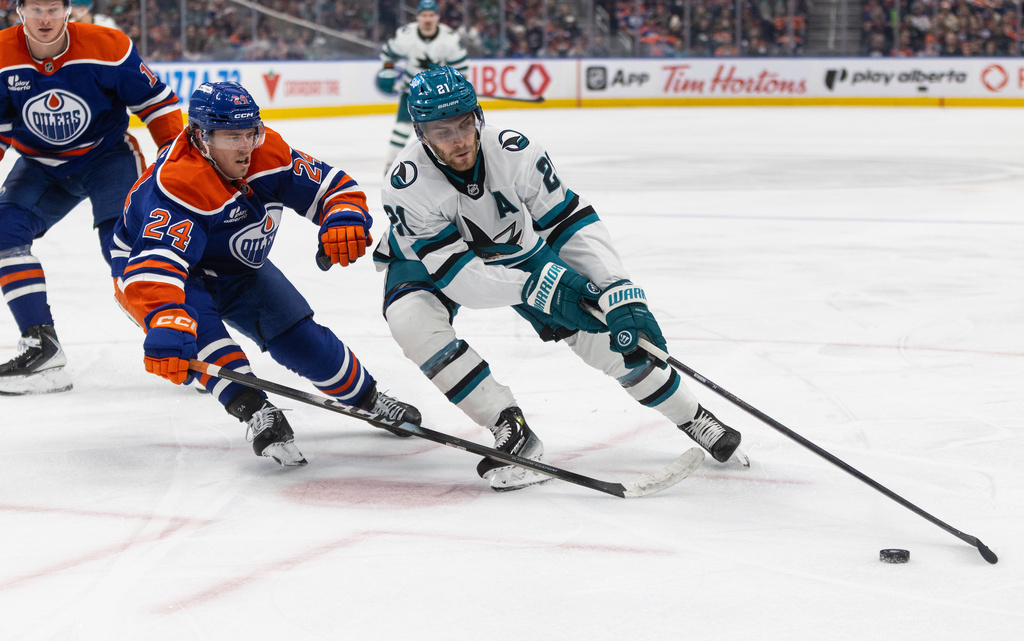 San Jose Sharks' Alex Wennberg (21) and Edmonton Oilers' Spencer Stastney (24) battle for the puck during third period NHL action, in Edmonton on Tuesday March 17, 2026. (Jason Franson/The Canadian Press via AP)