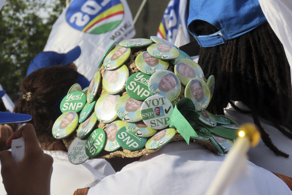A supporter wears a hat pinned with the symbols of the Seychelles National Party, a former opposition political party, during a campaign rally at Freedom Square in Victoria, Seychelles, Sunday, Sep. 21, 2025. (AP Photo/Emilie Chetty)