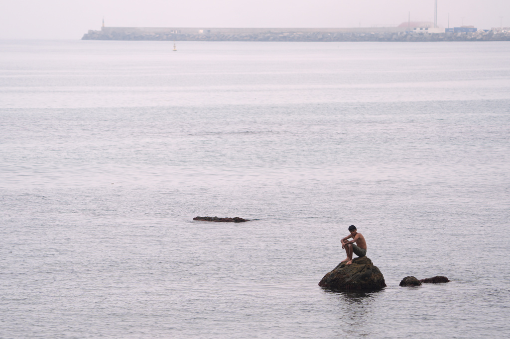 A migrant sits on a rock at El Trampolín beach in the Spanish exclave of Ceuta, Wednesday, Sept. 2, 2026. (AP Photo/Francis González)