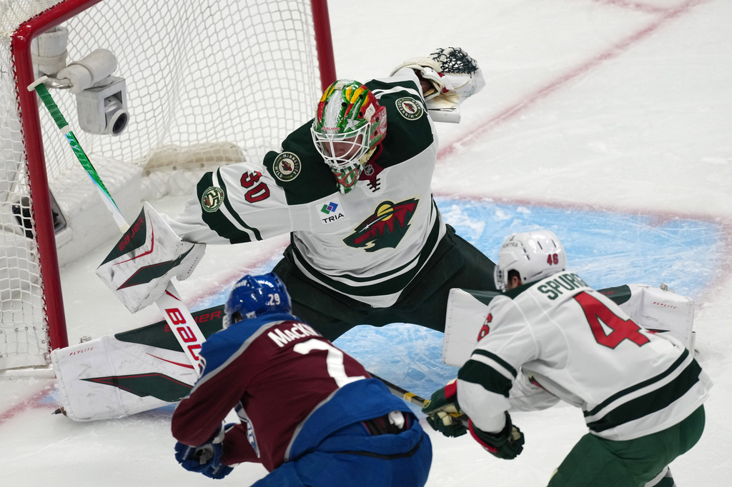 Colorado Avalanche center Nathan MacKinnon, front left, drives past Minnesota Wild defenseman Jared Spurgeon, right, to put a shot on goaltender Jesper Wallstedt in the first period of Game 1 of an NHL hockey Stanley Cup second-round playoff series, Sunday, May 3, 2026, in Denver. (AP Photo/David Zalubowski)