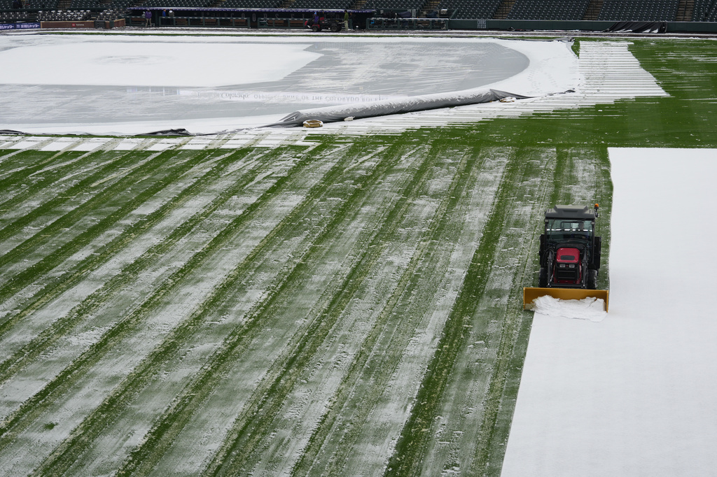 A grounds crew member clears snow from the outfield of Coors Field after a spring storm blanketed the intermountain West before the Colorado Rockies host the Los Angeles Dodgers Friday, April 17, 2026, in Denver. (AP Photo/David Zalubowski)