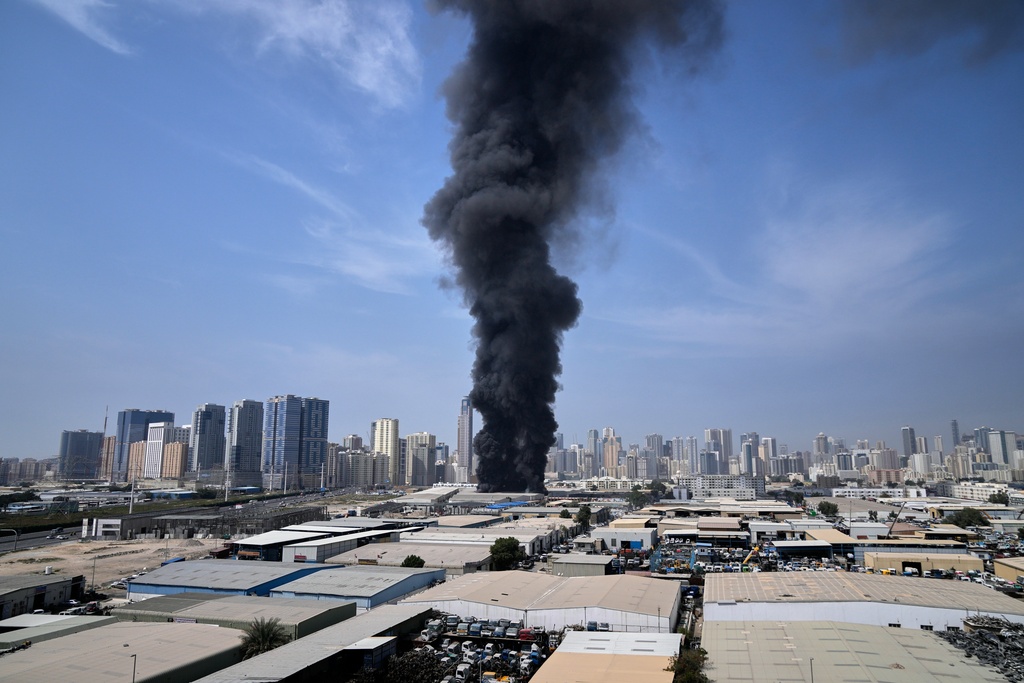 A black plume of smoke rises from a warehouse at the industrial area of Sharjah City in the United Arab Emirates following reports of Iranian strikes in Dubai, United Arab Emirates, Sunday, March 1, 2026. (AP Photo/Altaf Qadri)