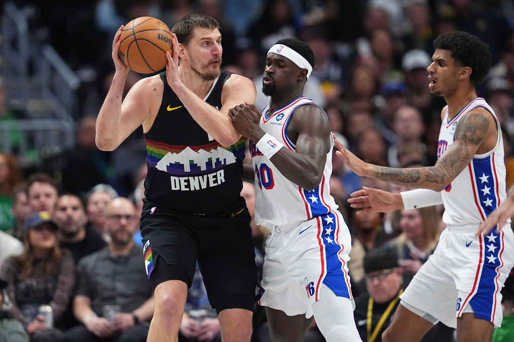 Denver Nuggets center Nikola Jokić, left, looks to pass the ball as Philadelphia 76ers forwards Adem Bona and Dominick Barlow, right, defend in the first half of an NBA basketball game Tuesday, March 17, 2026, in Denver. (AP Photo/David Zalubowski)