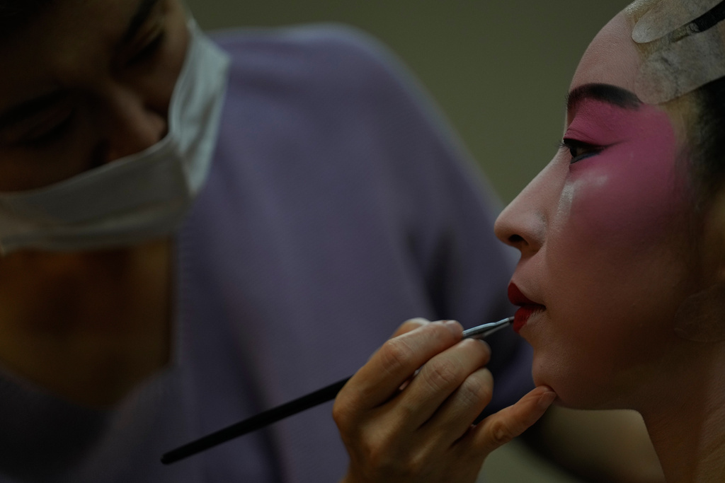 A makeup artist helps Peking Opera actress Zhang Wanting paint her face backstage before a performance at Jixiang Theatre in Beijing, China, Sunday, Sept. 7, 2025. (AP Photo/Mahesh Kumar A.)