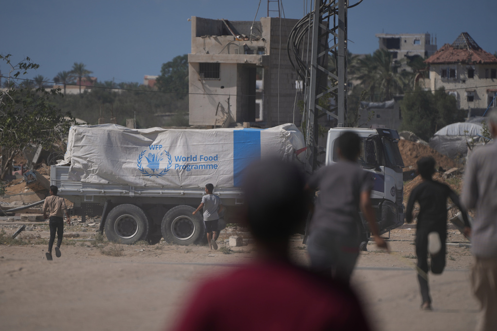 Palestinians rush toward trucks carrying aid from the World Food Programme (WFP) as they drive through Deir al-Balah in central Gaza, Wednesday, Oct. 15, 2025. (AP Photo/Abdel Kareem Hana)