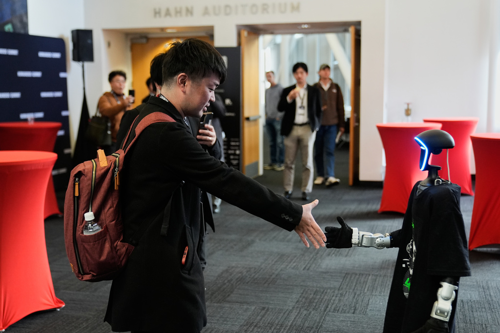 Kochi Sato, left, shakes hands with a humanoid robot during the Humanoids Summit, Thursday, Dec. 11, 2025, in Mountain View, Calif. (AP Photo/Godofredo A. Vásquez)