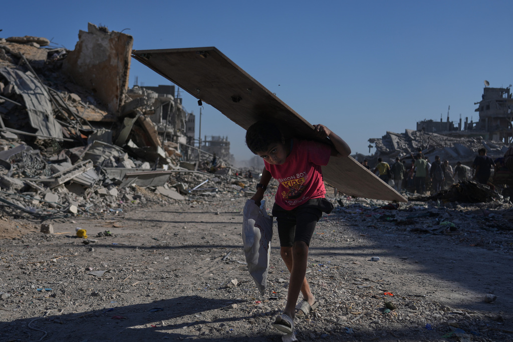 A displaced Palestinian boy carries a wooden board as he walks along the heavily damaged Al-Jalaa Street in Gaza City, Saturday, Oct. 11, 2025, after Israel and Hamas agreed to pause their war and release the remaining hostages. (AP Photo/Abdel Kareem Hana)