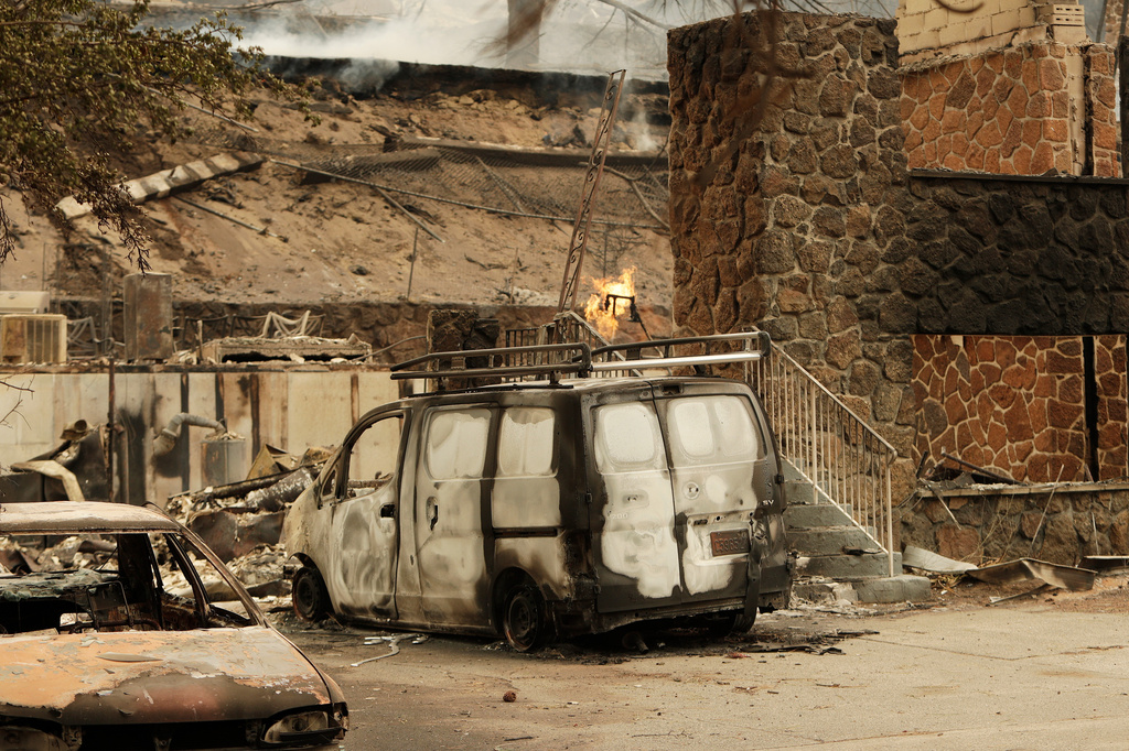 A charred van is parked by a building that burned down on W. Indian Trail Rd. in the aftermath of a wildfire in Spokane, Wash., Sunday, Aug. 2, 2026. (AP Photo/Young Kwak)