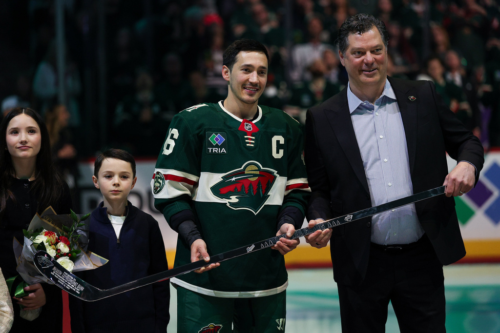 Minnesota Wild general manager Bill Guerin, right, and defenseman Jared Spurgeon pose photo with a silver stick honoring Spurgeon's 1,000 career games played in the NHL, prior to the Wild's NHL hockey game against the Dallas Stars Saturday, March 21, 2026, in St. Paul, Minn. (AP Photo/Matt Krohn)