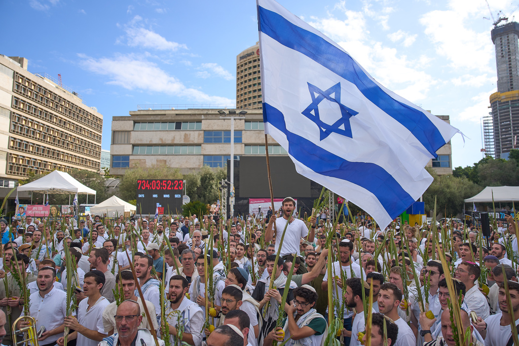 Covered in prayer shawls, men dance and hold the four items used as a symbol on the Jewish holiday of Sukkot, at a plaza known as hostages square following the announcement that Israel and Hamas have agreed to the first phase of a peace plan to pause the fighting in Gaza, in Tel Aviv, Israel, Friday, Oct. 10, 2025. (AP Photo/Ariel Schalit)
