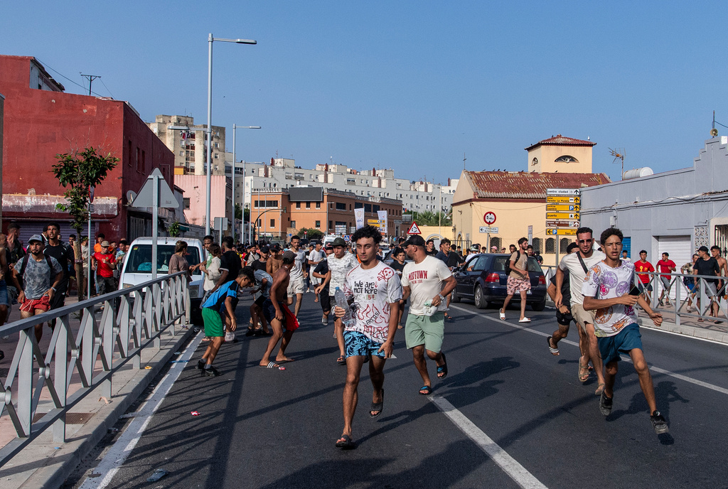 Migrants run from Spanish police officers after crossing from Morocco into the Spanish enclave of Ceuta, Friday, July 31, 2026. (AP Photo/Antonio Sempere)