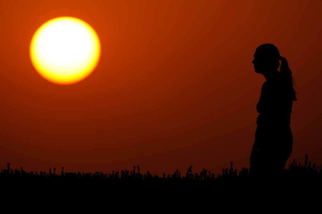 A woman watches the setting sun at the end of a hot summer day, Sunday, July 26, 2026, in Kansas City, Mo. (AP Photo/Charlie Riedel)