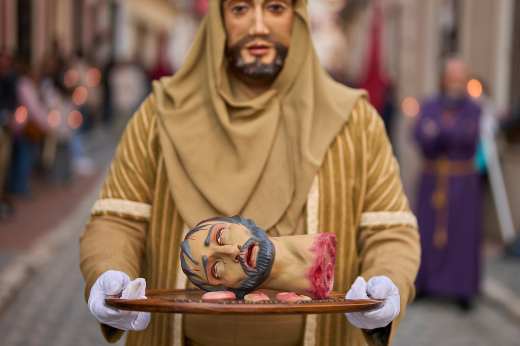 A penitent holds a tray with a figure's severed head, ears, and tongue depicting a biblical scene during a Holy Week procession of the "Hermandad de Nuestro Padre Jesus Nazareno" brotherhood in Puente Genil, southern Spain, Friday, April 3, 2026. (AP Photo/Manu Fernandez)