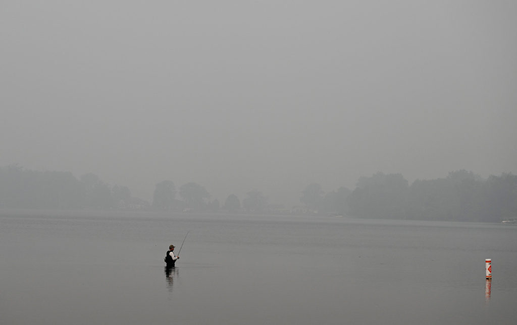 Wildfire smoke blankets Vandercook Lake as a fisherman tries his luck on Thursday, July 16, 2026, near Jackson, Mich., Thursday, July 16, 2026. (J. Scott Park/Jackson Citizen Patriot via AP)