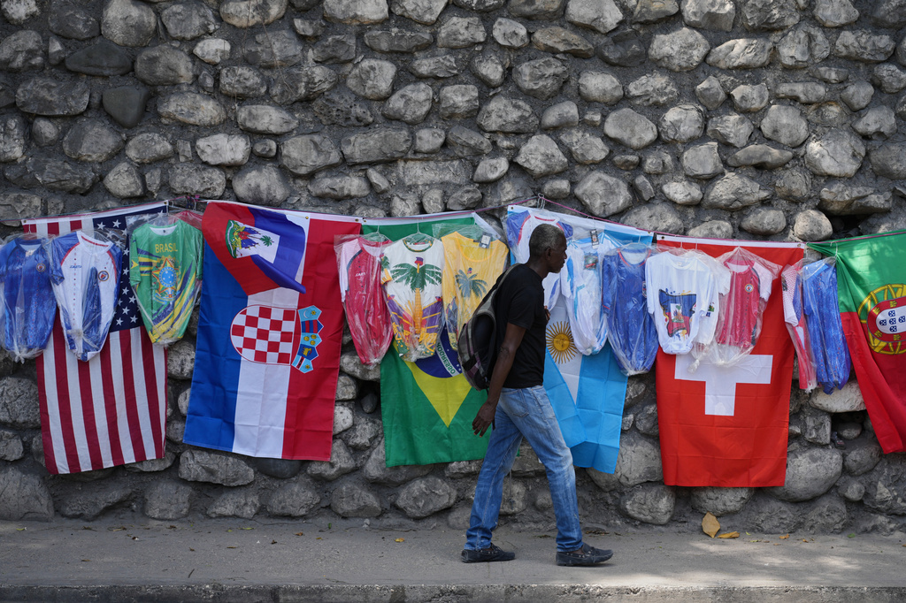 A pedestrian walks past flags and soccer jerseys for sale in a street in Port-au-Prince, Haiti, Wednesday, May 27, 2026. (AP Photo/Odelyn Joseph)