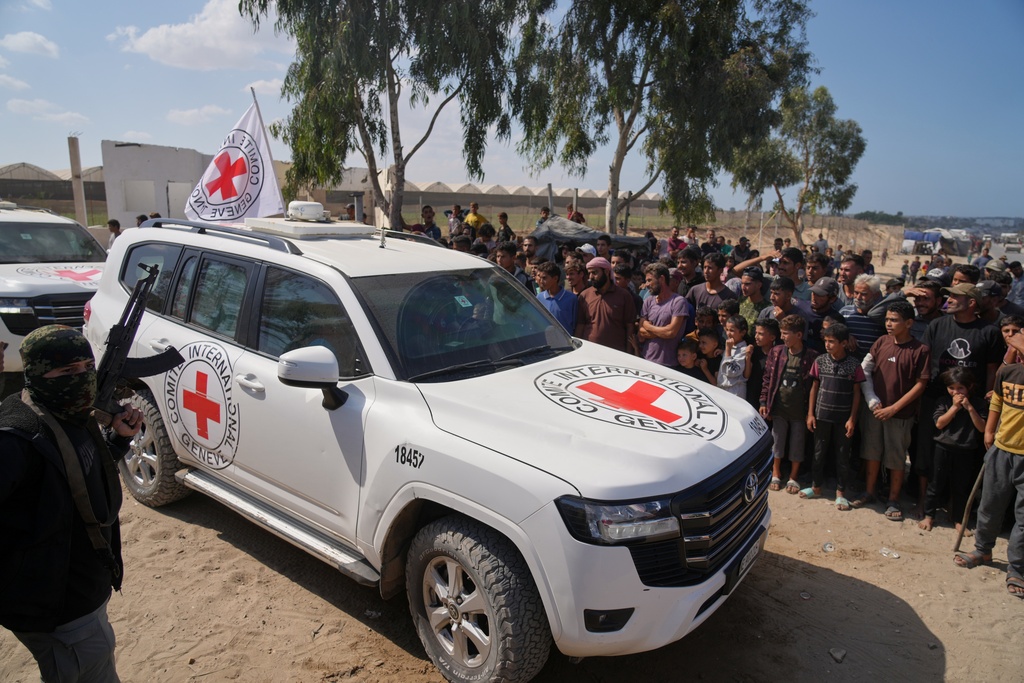 ICRC vehicles carrying released Israeli hostages make their way through groups of Palestinians and Hamas gunmen on their way to the Israeli border, in Khan Younis, southern Gaza Strip, Monday, Oct. 13, 2025. (AP Photo/Jehad Alshrafi)