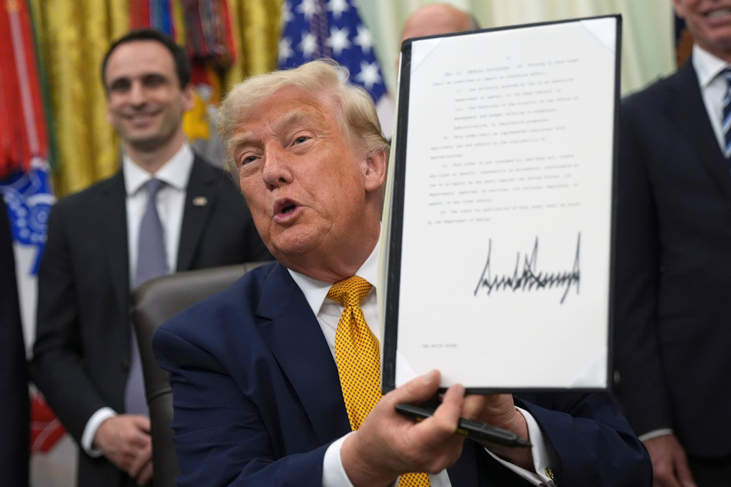 President Donald Trump holds up a signed executive order about quantum computing, in the Oval Office of the White House, Monday, June 22, 2026, in Washington. (AP Photo/Jacquelyn Martin)