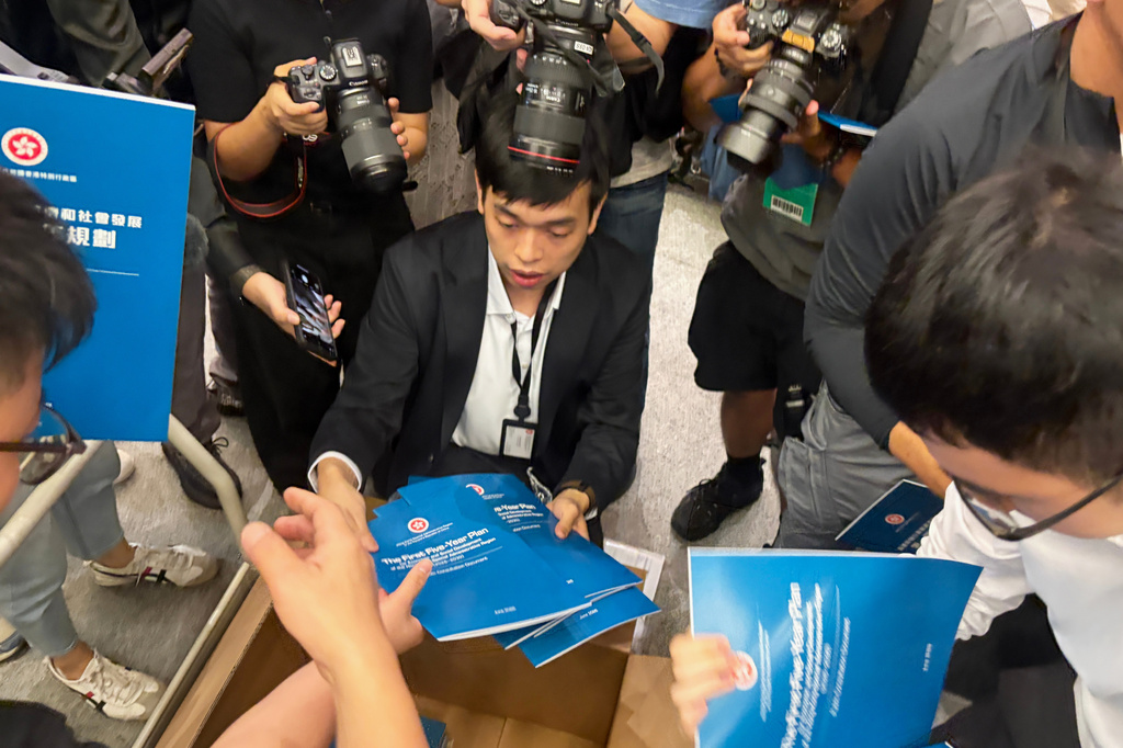 A man gives out copies of public consultation documents for Hong Kong's first five-year plan to reporters at the government headquarters in Admiralty district of Hong Kong, Monday, June 15, 2026. (AP Photo/Kanis Leung)