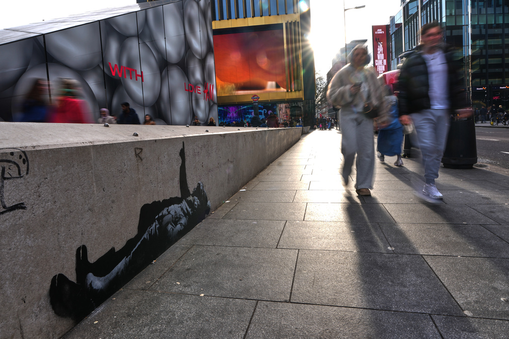 Pedestrians walk past a graffiti artwork, depicting two people, which recently appeared, outside Tottenham Court Road Station in London, Monday, Dec. 22, 2025 as elusive street artist Banksy appeared to confirm Monday that an identical image appeared on a wall on the side of a building in Bayswater, west London is his latest work. (AP Photo/Kirsty Wigglesworth)