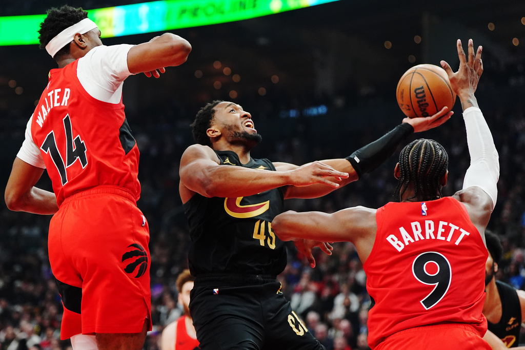 Cleveland Cavaliers' Donovan Mitchell (45) shoots as Toronto Raptors' Ja'kobe Walter (14) and RJ Barrett (9) defend during the first half of Game 6 in the first round of an NBA basketball playoffs series in Toronto on Friday, May 1, 2026. (Nathan Denette/The Canadian Press via AP)