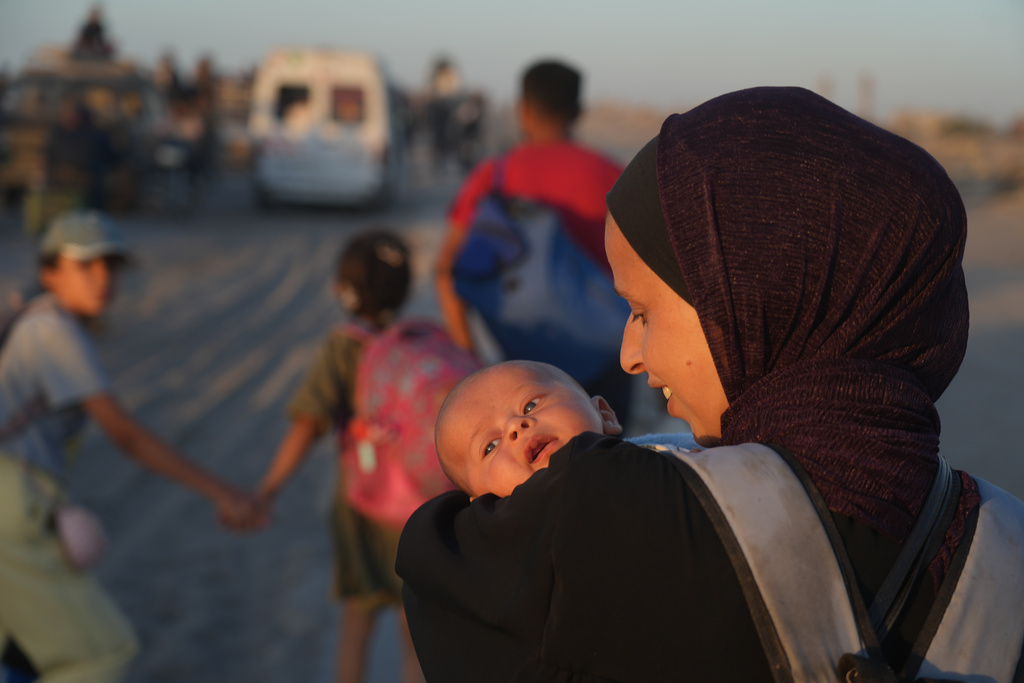 A displaced Palestinian woman carries her baby as she walks with others along the coastal road near Wadi Gaza in the central Gaza Strip, heading toward Gaza City, Friday, Oct. 10, 2025, after Israel and Hamas agreed to a pause in their war and the release of the remaining hostages. (AP Photo/Abdel Kareem Hana)
