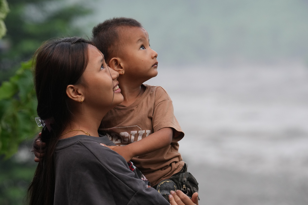 A girl holds a child as they watch a rescue helicopter fly by in Trishuli Bazaar area of Nuwakot district, Nepal, Sunday, Aug. 30, 2026. (AP Photo/Rajesh Kumar Singh)