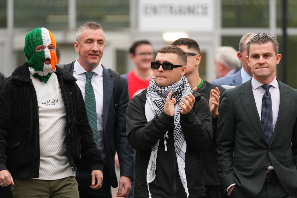 Liam Óg Ó hAnnaidh, aka Mo Chara, centre, a member of the Irish language band Kneecap, applauds as he leaves Woolwich Crown Court in London, Friday, Sept. 26, 2025, after Chief Magistrate, Senior District Judge Paul Goldspring, dismissed a terrorism offence relating to displaying a flag in support of Hezbollah during a performance with the band in November 2024, on a technical error. (AP Photo/Joanna Chan)