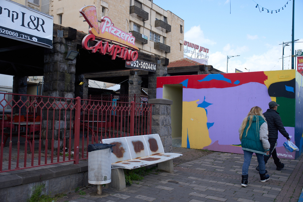People walk past a bomb shelter next to closed shops in Kiryat Shmona, northern Israel, on the border with Lebanon, Monday, March 16, 2026. (AP Photo/Ariel Schalit)