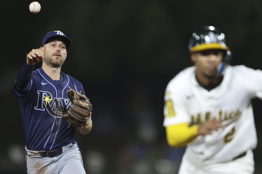 Tampa Bay Rays second baseman Brandon Lowe, left, throws to third as Athletics' Darell Hernaiz, right is called out during a rundown during the eighth inning of a baseball game Tuesday, Aug. 12, 2025, in West Sacramento, Calif. (AP Photo/Scott Marshall)