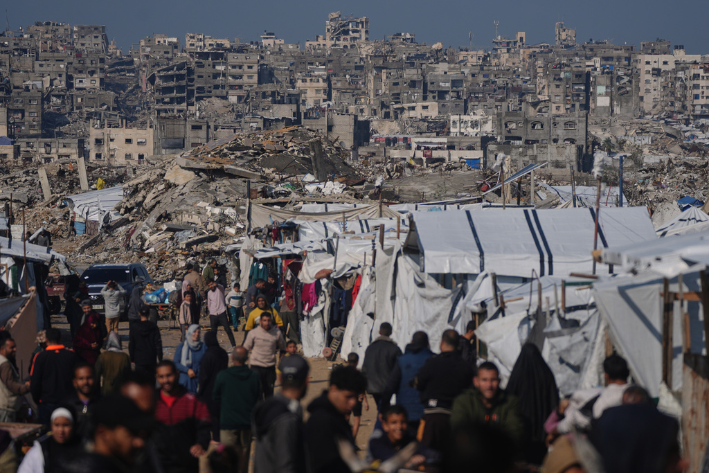 Palestinians walk along a street past a tent camp, backdropped by buildings destroyed during Israeli air and ground operations in Gaza City, Wednesday, Dec. 17, 2025. (AP Photo/Jehad Alshrafi)