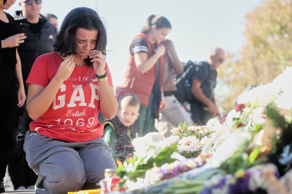A woman cries before lighting a candle by floral tributes outside the train station on the first anniversary of the disaster that killed 16 people, in Novi Sad, Serbia, Saturday, Nov. 1, 2025. (AP Photo/Armin Durgut)