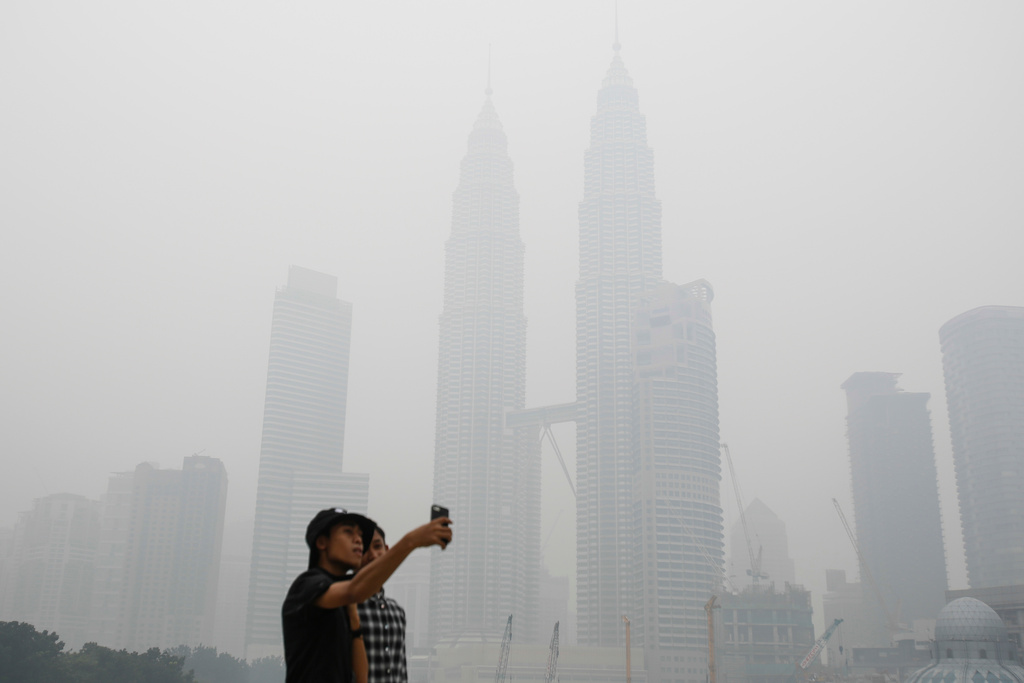 FILE -Tourists take a selfie against Malaysia's landmark building Petronas Twin Towers shrouded with haze in Kuala Lumpur, Malaysia on Sept. 26, 2015. (AP Photo/Joshua Paul, File)