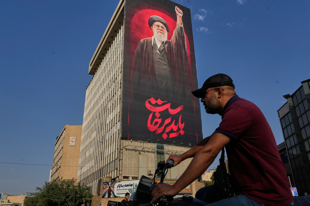 A man rides on his motorbike past a billboard with a message that reads in Farsi: " We must rise up" and an image of the late Iranian Supreme Leader Ayatollah Ali Khamenei, who was killed during the U.S. and Israel strikes on Feb. 28, in Tehran, Iran, Saturday, Aug. 15, 2026. (AP Photo/Vahid Salemi)