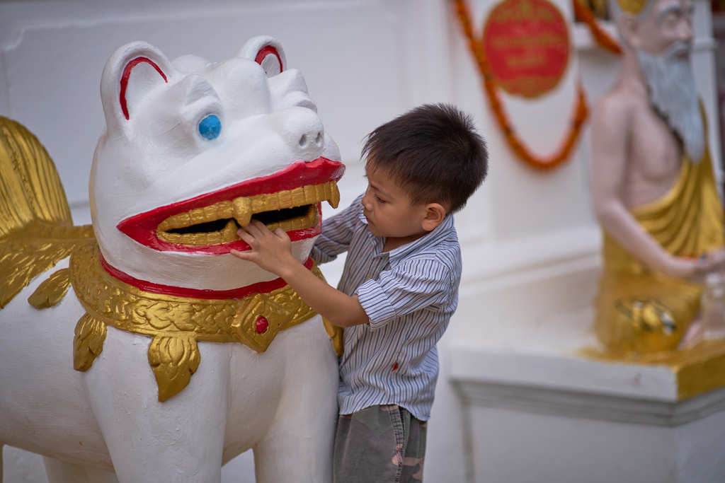 A child plays with a temple guardian statue outside a Buddhist temple in Luang Prabang, Laos, Sunday, Nov. 2, 2025. (AP Photo/Eugene Hoshiko)