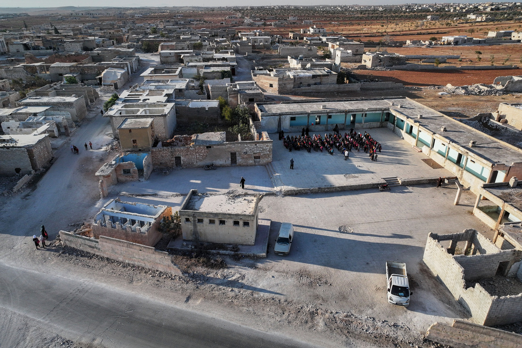 Students gather in the courtyard of the Maar Shmarin Primary School, surrounded by houses destroyed during the fighting between forces loyal to former President Bashar Assad and rebel groups, in the village of Maar Shmarin, in the Idlib countryside, Syria, Sunday, Oct. 19, 2025. (AP Photo/Ghaith Alsayed)