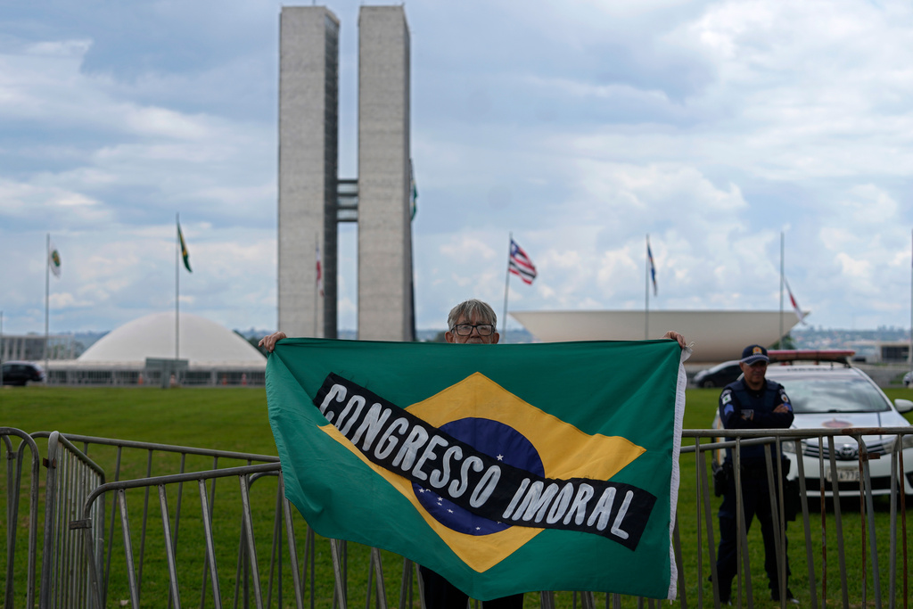 A demonstrator carries a Brazilian flag with the phrase, "Immoral Congress" in Portuguese in front of Congress during a protest against a bill that looks to reduce former President Jair Bolsonaro's prison time, in Brasilia, Brazil, Sunday, Dec. 14, 2025. (AP Photo/Eraldo Peres)