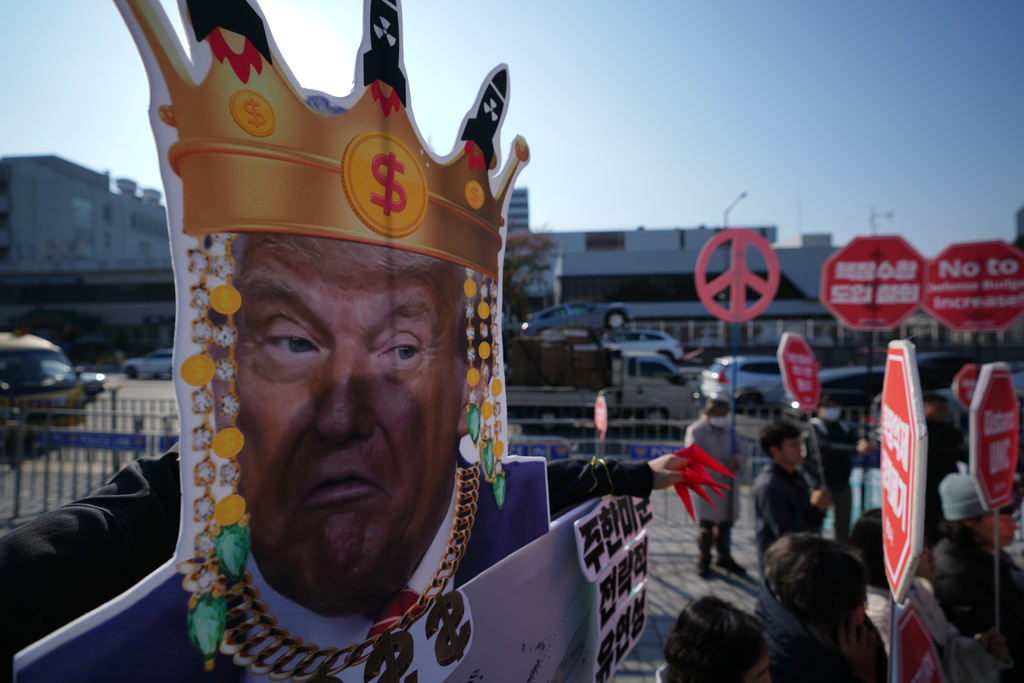 A protester wearing a mask of U.S. President Donald Trump stands near others during a rally to oppose the South Korea plan to acquire nuclear-powered submarines while gathering near the Defense Ministry in Seoul, South Korea, Tuesday, Nov. 4, 2025. (AP Photo/Lee Jin-man)