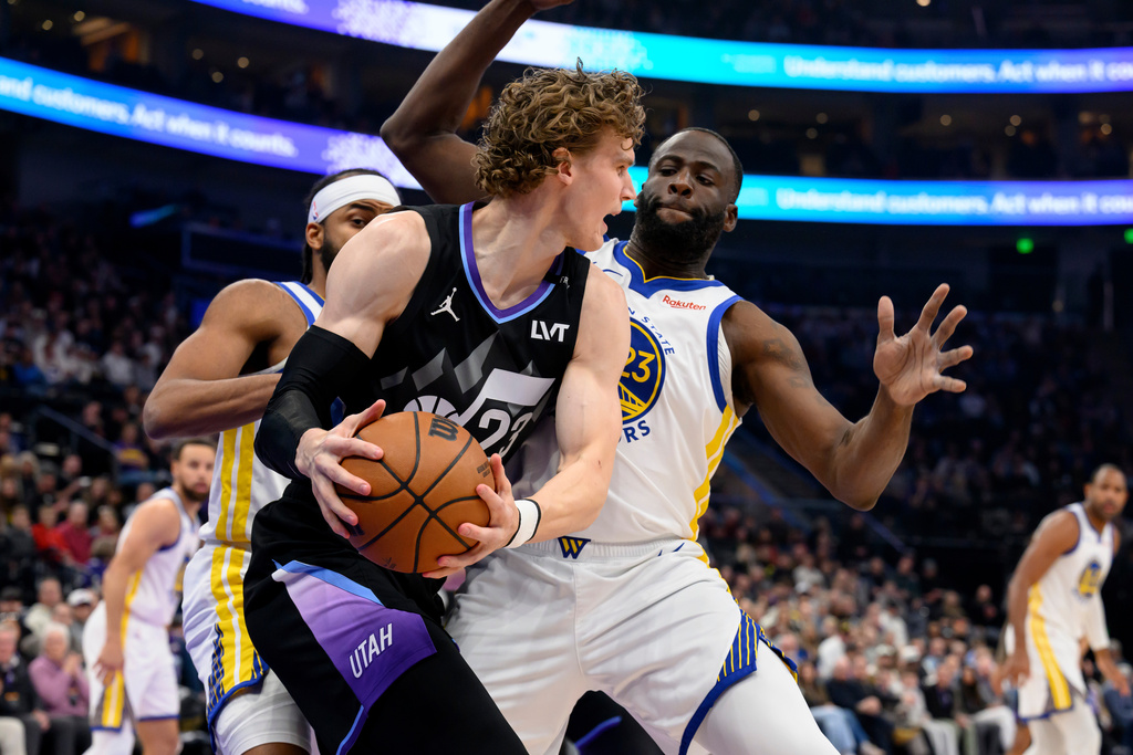 Utah Jazz forward Lauri Markkanen, center front, looks to pass around the defense of Golden State Warriors forward Draymond Green, center right, during the first half of an NBA basketball game, Wednesday, Jan. 28, 2026, in Salt Lake City. (AP Photo/Tyler Tate)