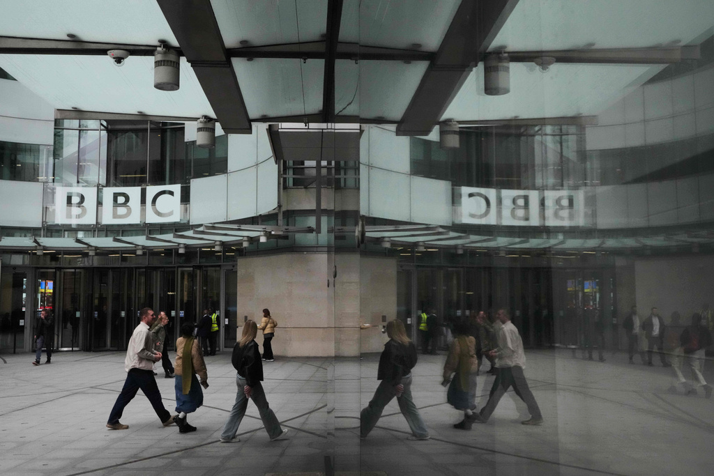 Pedestrians are reflected as they walk outside BBC Broadcasting House in London, Tuesday, Nov. 11, 2025. (AP Photo/Kirsty Wigglesworth)