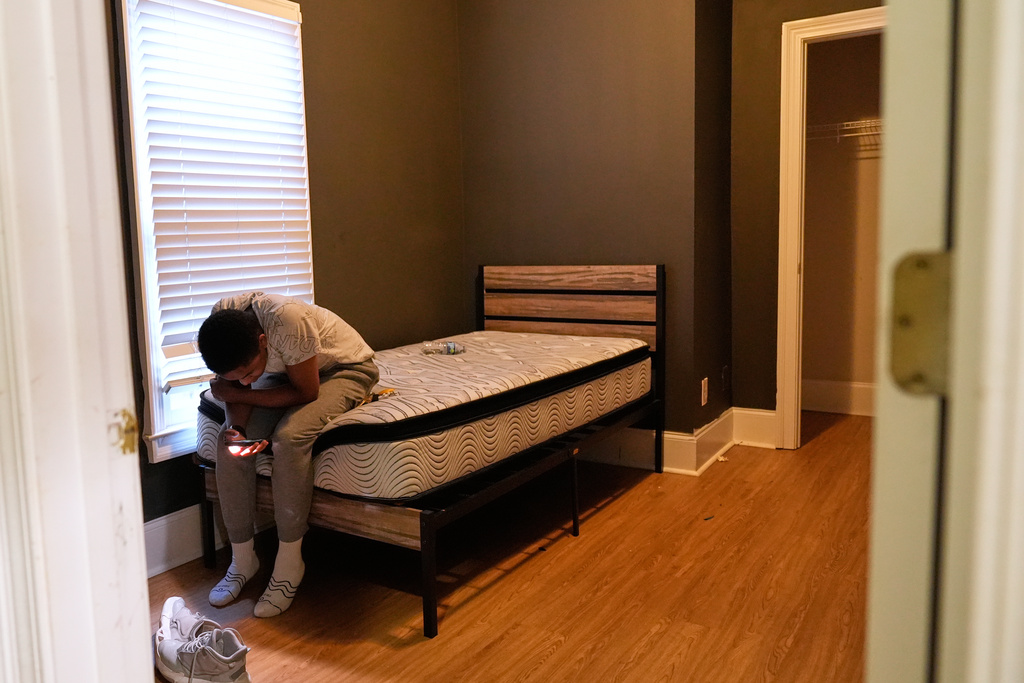 Elias Washington watches a video on his phone as he rests on a bed left by a previous tenant in his family's new apartment in Atlanta on Aug. 1, 2025. (AP Photo/Brynn Anderson)