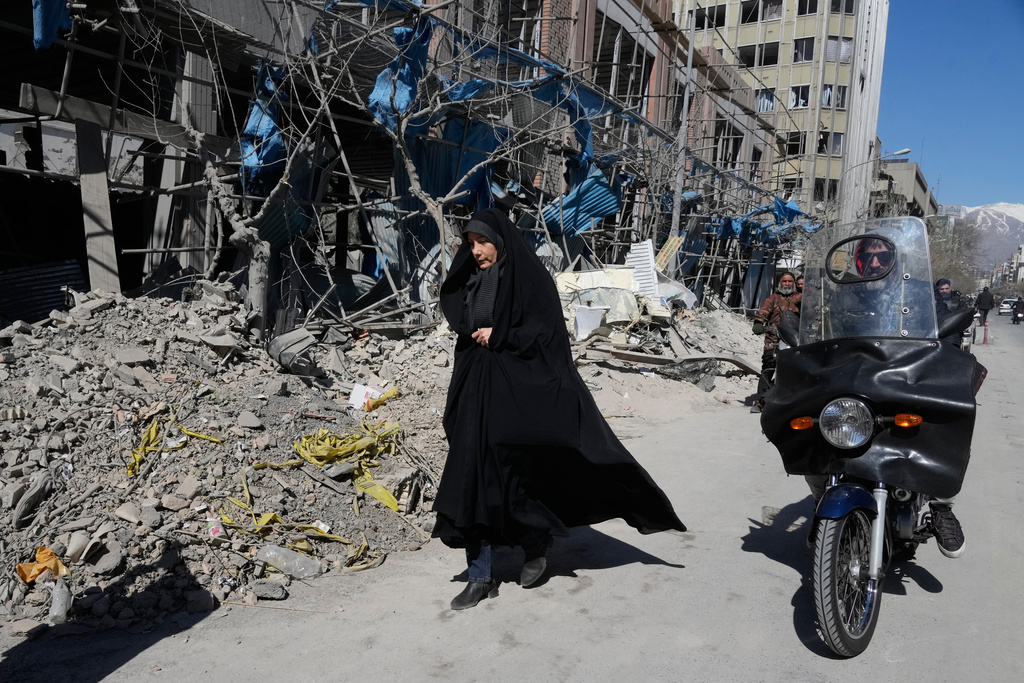 A woman walks past a building which was damaged after a strike on a police station amid the U.S.–Israeli military campaign in Tehran, Iran, Tuesday, March 3, 2026. (AP Photo/Vahid Salemi)